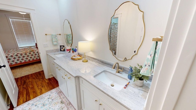 ensuite bathroom featuring double vanity, a sink, ensuite bath, and wood finished floors