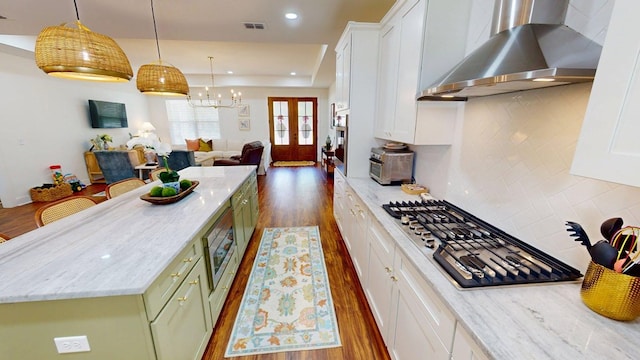 kitchen featuring stainless steel gas stovetop, dark wood-style flooring, white cabinets, green cabinetry, and wall chimney range hood
