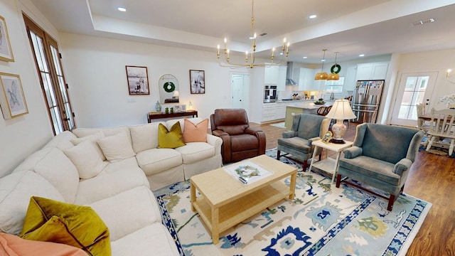 living area featuring an inviting chandelier, light wood-style flooring, a tray ceiling, and visible vents