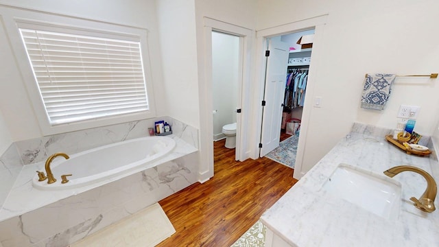 full bathroom with vanity, a walk in closet, toilet, a garden tub, and wood finished floors