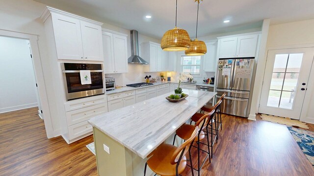kitchen with a breakfast bar, appliances with stainless steel finishes, dark wood-type flooring, and wall chimney exhaust hood