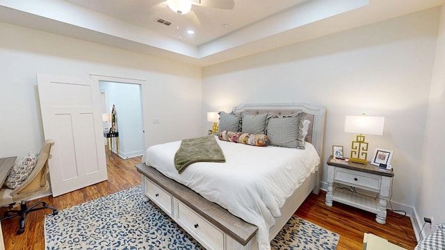 bedroom with baseboards, visible vents, wood finished floors, and a raised ceiling
