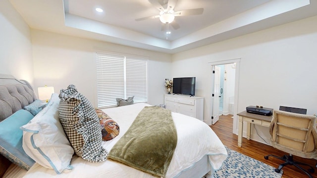 bedroom featuring a tray ceiling, a ceiling fan, wood finished floors, ensuite bathroom, and recessed lighting