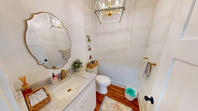 bathroom featuring a notable chandelier, toilet, vanity, wood finished floors, and baseboards