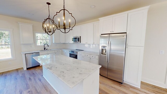 kitchen with pendant lighting, sink, white cabinetry, stainless steel appliances, and a kitchen island