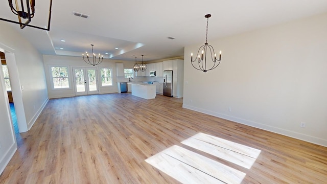 unfurnished living room featuring sink, light hardwood / wood-style flooring, a notable chandelier, a raised ceiling, and french doors