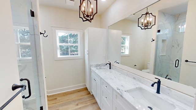 bathroom with toilet, vanity, a shower with door, a notable chandelier, and hardwood / wood-style floors