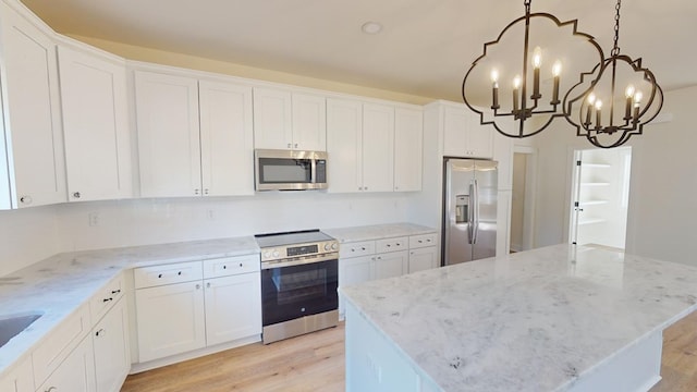 kitchen with a kitchen island, appliances with stainless steel finishes, decorative light fixtures, white cabinetry, and light stone counters