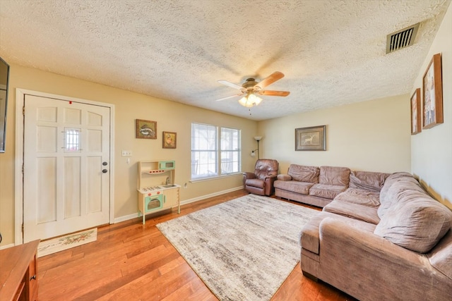 living room with a textured ceiling, ceiling fan, and light wood-type flooring