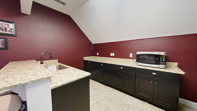 kitchen featuring light stone countertops, lofted ceiling, a kitchen island with sink, and sink