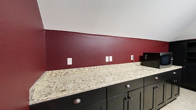 kitchen featuring lofted ceiling and light stone counters