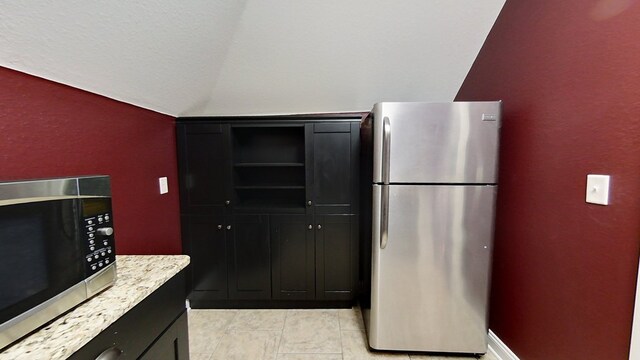 kitchen with light stone countertops, vaulted ceiling, and stainless steel appliances