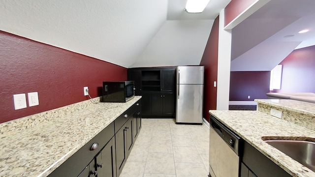 kitchen with light stone counters, stainless steel appliances, light tile patterned flooring, and vaulted ceiling