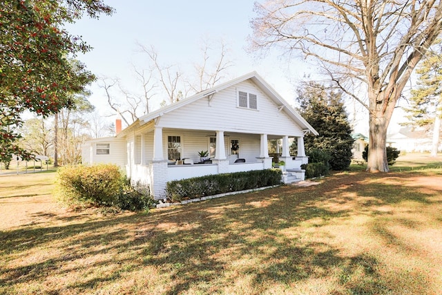 bungalow featuring a porch, a front lawn, and a chimney