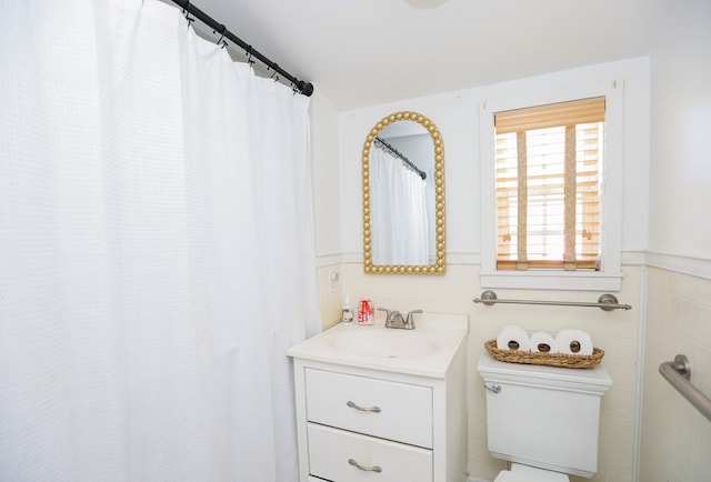 full bathroom featuring toilet, wainscoting, vanity, and tile walls