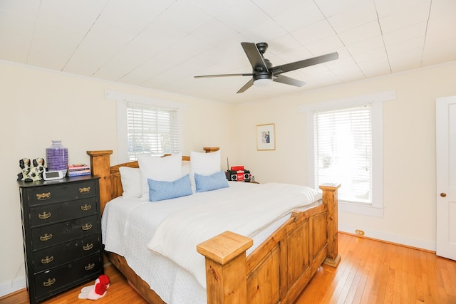 bedroom featuring light wood finished floors, crown molding, baseboards, and a ceiling fan