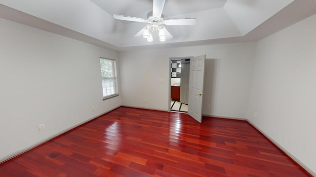 empty room featuring a raised ceiling, dark wood-type flooring, and ceiling fan