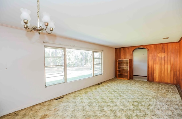 unfurnished room with ornamental molding, light carpet, an inviting chandelier, and wood walls