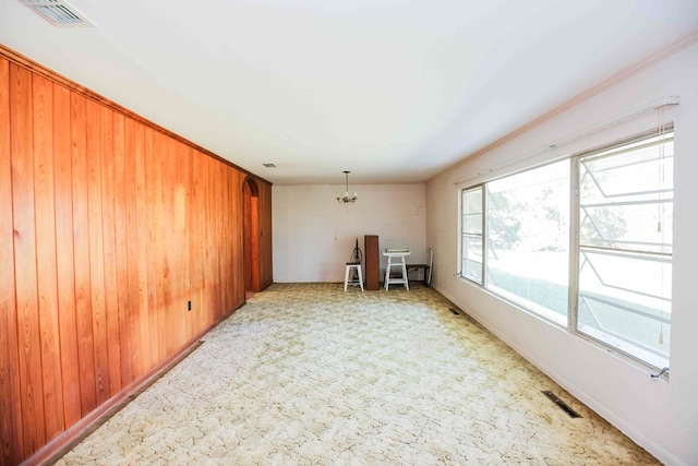 carpeted spare room featuring an inviting chandelier and wood walls