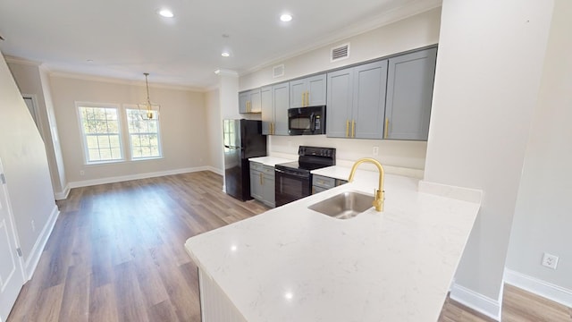 kitchen featuring decorative light fixtures, black appliances, sink, light stone counters, and kitchen peninsula