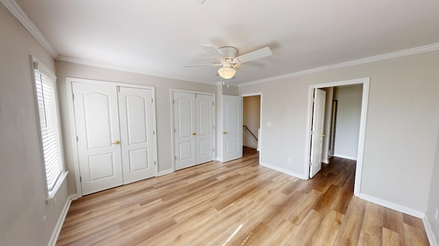 unfurnished bedroom featuring ceiling fan, ornamental molding, light hardwood / wood-style flooring, and two closets