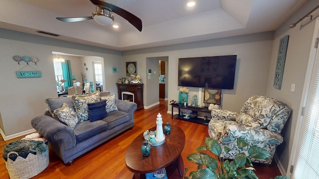 living room with ceiling fan, a tray ceiling, and hardwood / wood-style floors