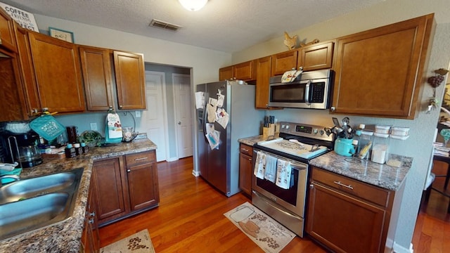 kitchen with sink, appliances with stainless steel finishes, dark hardwood / wood-style floors, a textured ceiling, and stone countertops