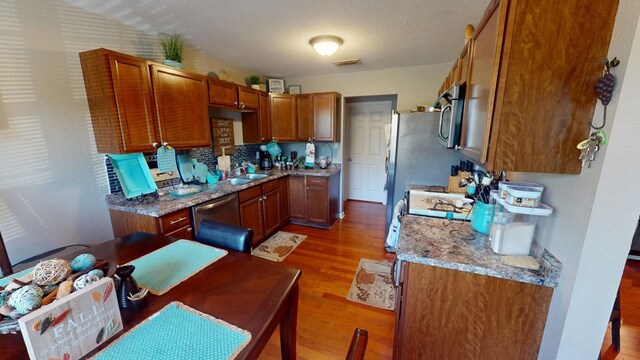 kitchen with sink, appliances with stainless steel finishes, wood-type flooring, light stone countertops, and a textured ceiling