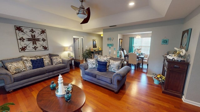 living room featuring hardwood / wood-style floors, ceiling fan, and a tray ceiling