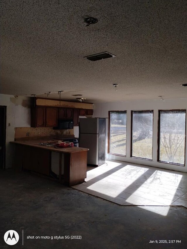 kitchen featuring a peninsula, plenty of natural light, black microwave, and freestanding refrigerator