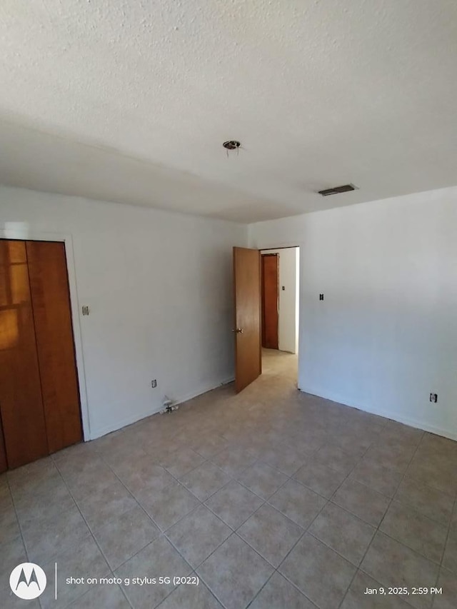 empty room with light tile patterned floors, visible vents, and a textured ceiling