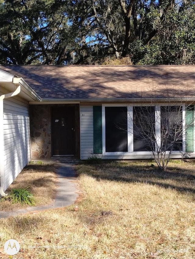 doorway to property featuring a shingled roof, stone siding, and a lawn