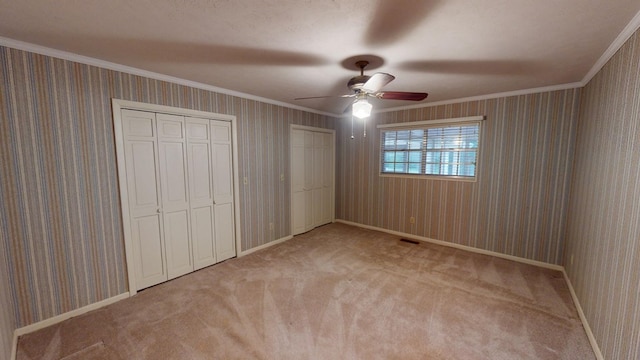 unfurnished bedroom with multiple closets, ornamental molding, light colored carpet, and ceiling fan