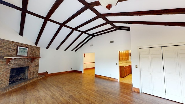 unfurnished living room with beamed ceiling, wood-type flooring, and a brick fireplace