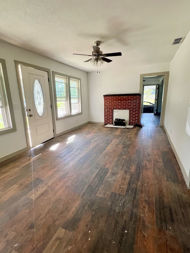 unfurnished living room with dark wood-type flooring, ceiling fan, a fireplace, and a textured ceiling