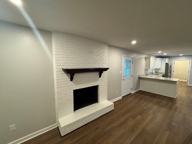 unfurnished living room featuring dark hardwood / wood-style flooring, sink, and a brick fireplace