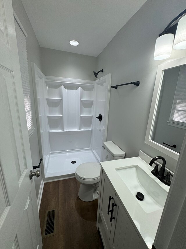 bathroom with hardwood / wood-style flooring, vanity, toilet, and walk in shower