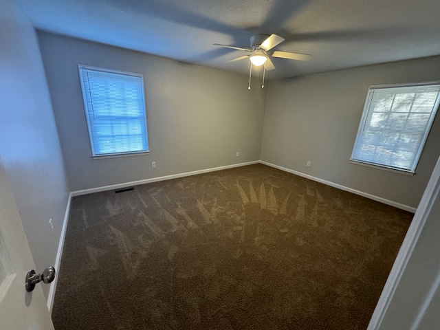 unfurnished room featuring ceiling fan, a healthy amount of sunlight, and dark carpet