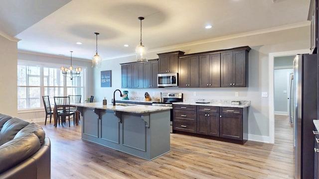 kitchen with sink, pendant lighting, stainless steel appliances, light stone countertops, and a kitchen island with sink