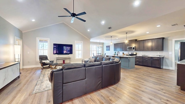 living room with light hardwood / wood-style flooring, sink, ceiling fan with notable chandelier, high vaulted ceiling, and ornamental molding