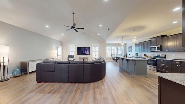 living room featuring ceiling fan with notable chandelier, high vaulted ceiling, sink, and light wood-type flooring