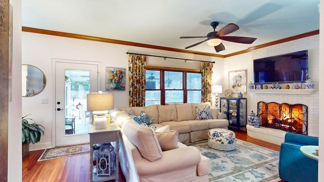 living room with ornamental molding, a ceiling fan, a fireplace, and wood finished floors