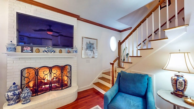 interior space featuring stairway, ornamental molding, a brick fireplace, wood finished floors, and baseboards