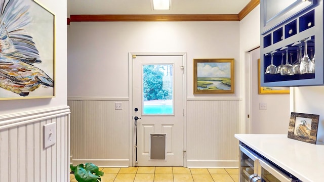 doorway featuring light tile patterned floors, wainscoting, and crown molding