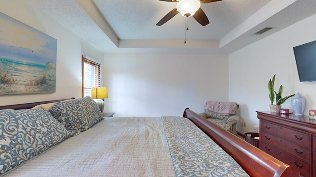 bedroom featuring a ceiling fan, visible vents, a raised ceiling, and a textured ceiling