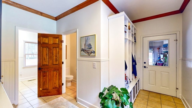 foyer entrance featuring a wainscoted wall, ornamental molding, and light tile patterned flooring