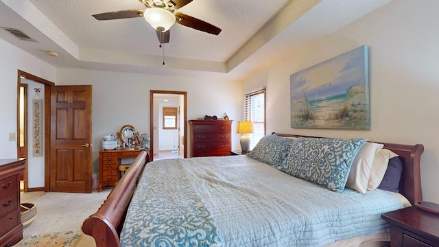 bedroom with light carpet, visible vents, baseboards, a ceiling fan, and a tray ceiling