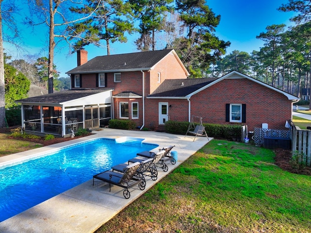 back of house featuring a chimney, a lawn, a sunroom, a patio area, and an outdoor pool