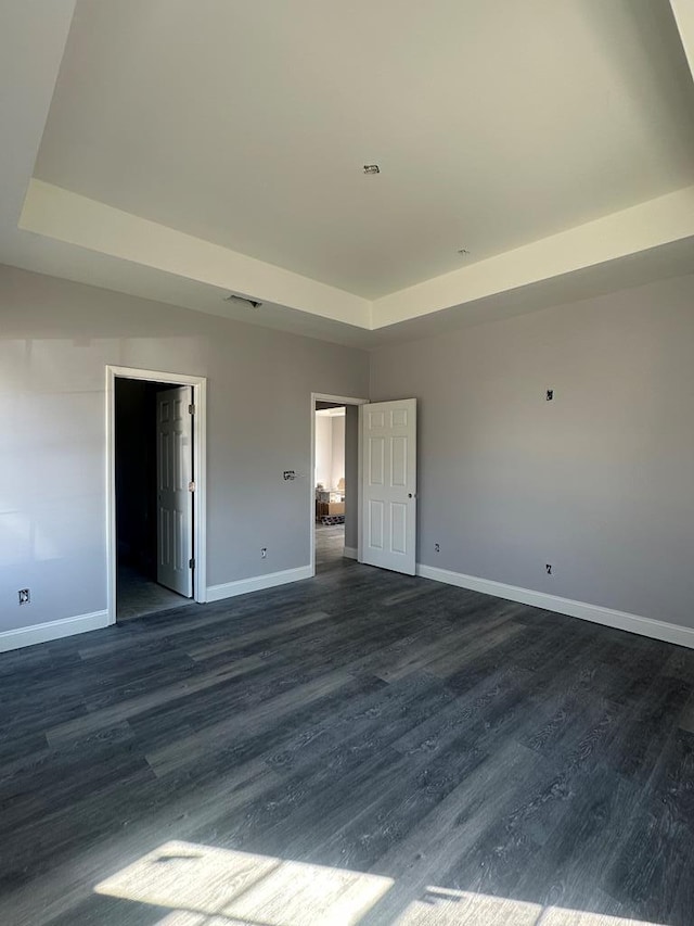 unfurnished bedroom with a tray ceiling, dark wood finished floors, and baseboards