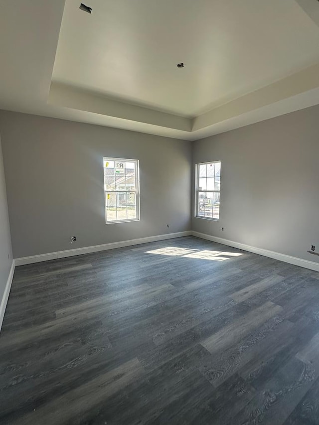 unfurnished room with dark wood-style floors, a raised ceiling, and baseboards